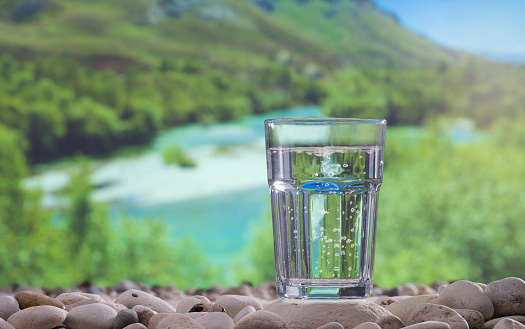 Glass of water on stones and river in background