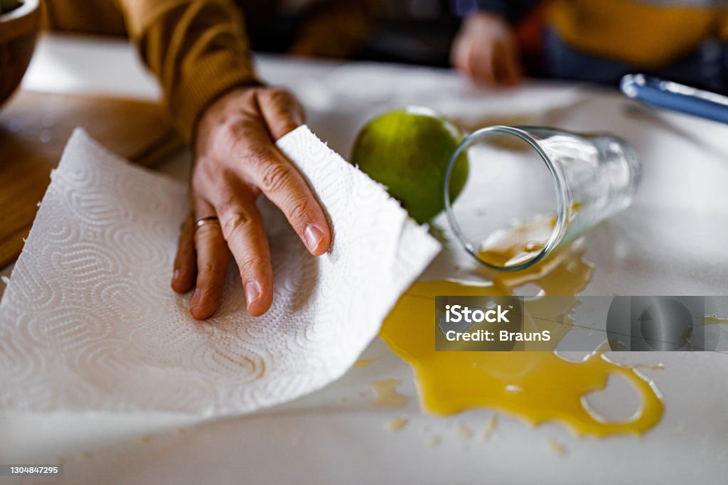 Cleaning spilled orange juice! Close up of unrecognizable man cleaning spilled juice from the table. Spilling Stock Photo