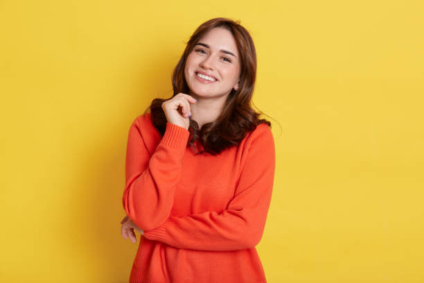 istock Happy smiling dark haired woman with pleasant appearance, wearing casually, looking at camera with toothy smile, keeping fist under chin, standing isolated over yellow background. 1304850049