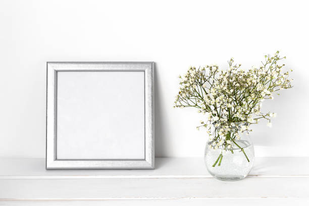 istock White spring flowers in a glass vase with a silver photo frame on a white table. Cozy white interior 1304851352