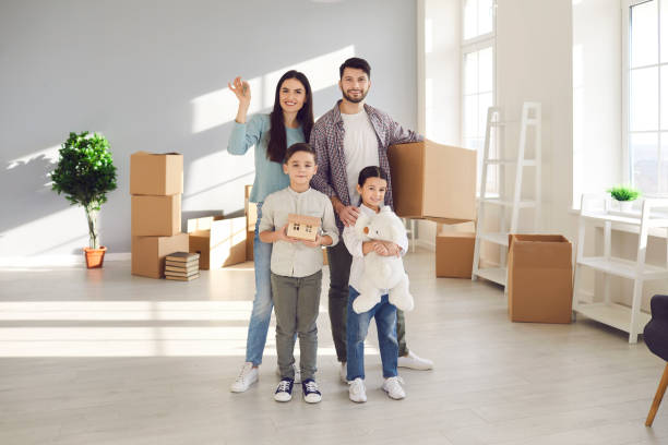 Young happy family with children enjoying new apartment together Young happy family with children boy and girl standing together and holding boxes with belongings in new spacious apartment after relocating. Renting buying or moving to new accomodation concept happy family with key of their new house stock pictures, royalty-free photos & images