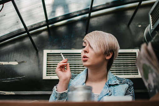 Portrait of a young beautiful blondie enjoying smoking in a cafe