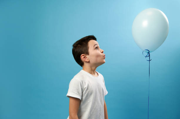 istock Cute schoolboy looking at a blue balloon on blue background 1304853454