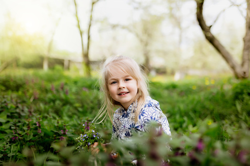 Little smiling girl with spring flowers on green lawn in the garden. High quality photo