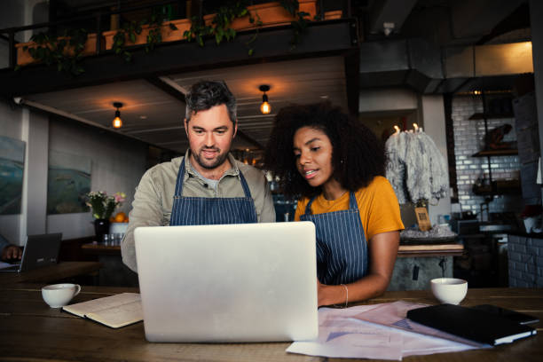 istock Manager and waitress deciding on construction work of cafe sitting with laptop and paper work in trendy coffee shop 1304854279