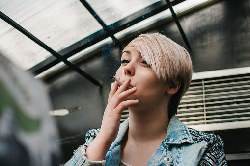Portrait of a young short-haired woman smoking cigarettes in a cafe. A cigarette addict who enjoys smoking