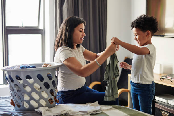 A little progress everyday adds  to big things Shot of a young mother sitting on a bed helping her your son fold laundry task stock pictures, royalty-free photos & images