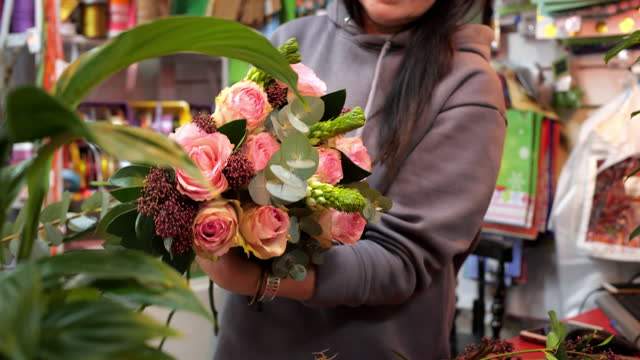Woman florist creating rose bouquet at flower shop. Portrait female seller making gift bouquet from roses in flower boutique. Small business flower workshop concept.
