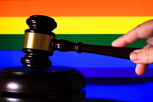 Hand holding Judge wooden mallet and colorful rainbow flag in the background