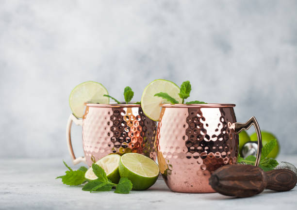 istock Moscow mule cocktail in a copper mug with lime and mint and wooden squeezer on light background 1304862748