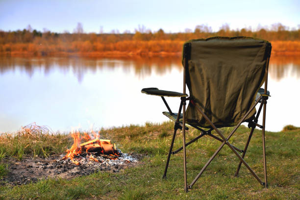 touristenstuhl, klappstuhl, lagerfeuer am flussufer im herbst bei sonnenuntergang, entspannung und erholung, frühherbst, nahaufnahme, kopierraum - campingstuhl stock-fotos und bilder