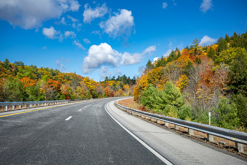 A mesmerizing landscape that attracts tourists with a stretching into the horizon highway road framed by picturesque autumn red and yellow maples in the state of Vermont in New England