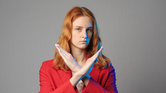 Young caucasian redhead woman in red jacket rejection hands crossed isolated on grey copyspace