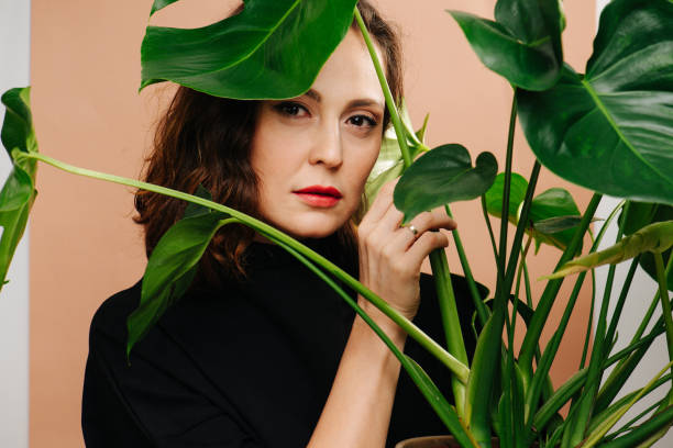 istock Sensual middle aged woman looking at camera from behind monstera plant 1304865497