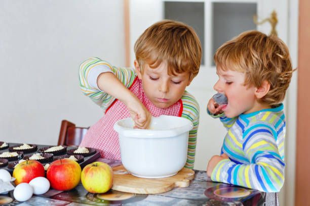 two little funny brothers baking apple cake in domestic kitchen. happy healthy kid boys having fun with working with mixer, eggs and fruits. children tasting dough indoors - smiling little girls little boys autumn imagens e fotografias de stock