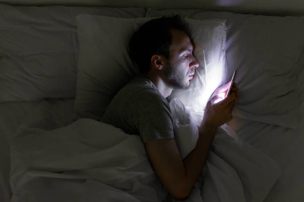 Bored man chatting and surfing on internet with smartphone late at night Mobile addiction, nomophobia, insomnia, sleep disorder concept. Bored man chatting and surfing on internet with smart phone late at night, lying on bed under the blanket. man sleeping top view stock pictures, royalty-free photos & images