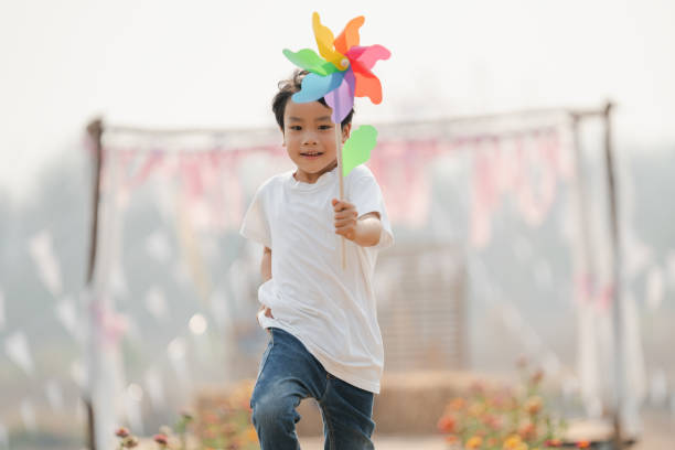 istock boy holding a toy windmill happily runing in the park 1304870147