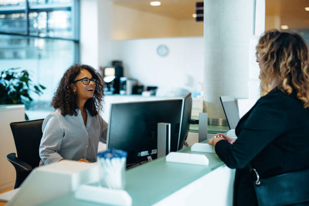 Friendly administrator assisting woman at reception desk Receptionist assisting a woman standing at front desk. Woman standing at the reception talking with a friendly receptionist behind the desk of municipality office. politics and government stock pictures, royalty-free photos & images