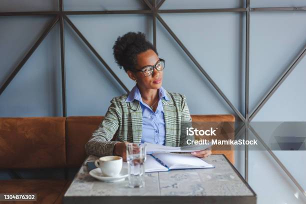 Black businesswoman brainstorming while working on documents in a cafe.