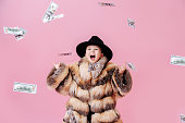 Playful little boy in fur coat making rock'n roll gesture under money rain