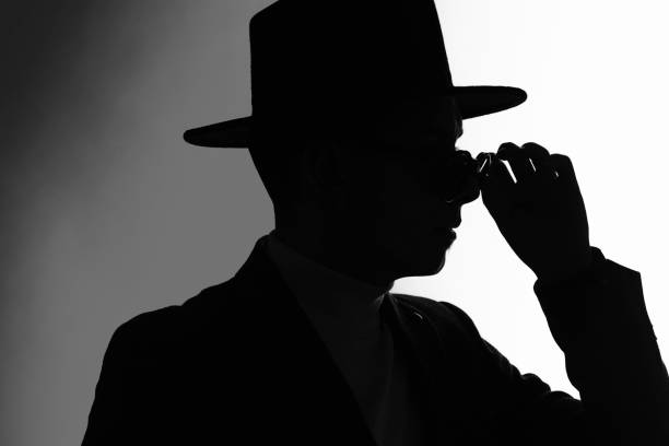 istock Silhouette of a man in a jacket and classial hat fixing sunglasses 1304879032