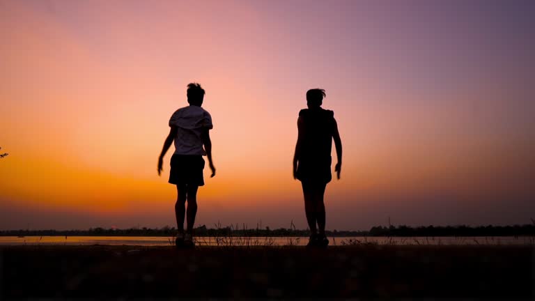 Silhouetted fitness man doing jumping jacks or star jump exercise at seaside outdoors on sunset ,full length portrait.