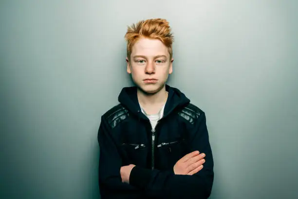 Young teenage boy standing with arms crossed and looking confidently into the camera with a decisive look