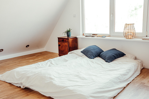 Minimalist white bed mattress on solid hardwood oak floor in cozy modern home bedroom. Minimalist white bright room.