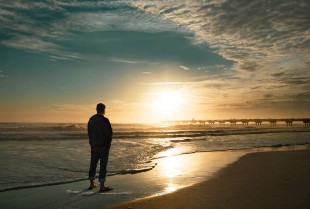 Man standing on the beach looking at sunrise. Sun rising over the pier. Jacksonville, Florida, USA.