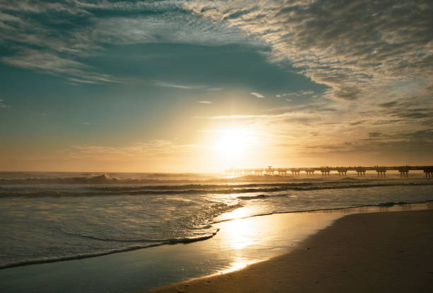 Sun rising over horizon and pier, beach illuminated with sunlight. Jacksonville Florida, USA.