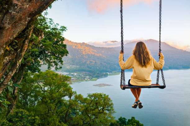 Young woman looking at amazing tropical lake in mountains Summer vacation. Young woman sit on tree rope swing on high cliff above tropical lake. Happy girl looking at amazing jungle view. Buyan lake is popular travel destinations in Bali island, Indonesia swinging stock pictures, royalty-free photos & images