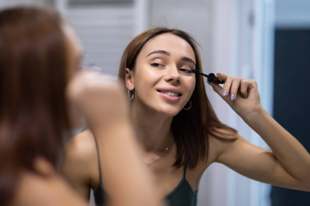 istock Beautiful young woman using mascara in bathroom 1304889160
