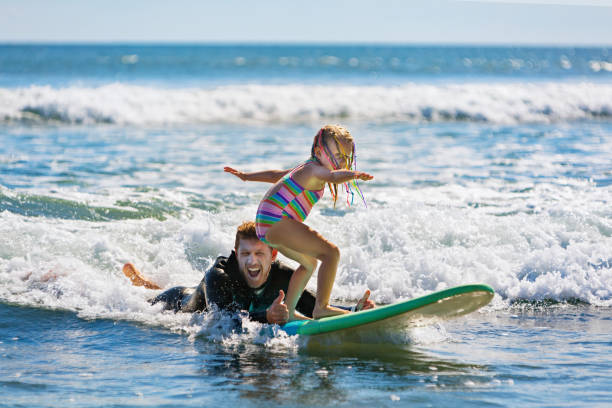 joven surfista aprende a montar en tabla de surf con instructor de surf - surfing beach family father fotografías e imágenes de stock