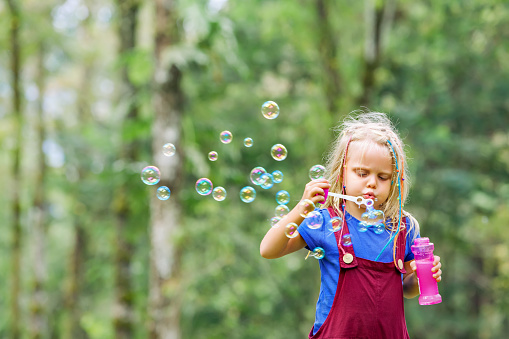 Happy girl playing with soap bubbles. Active child walking in the park. Family lifestyle, outdood activities, summer holidays with kids.