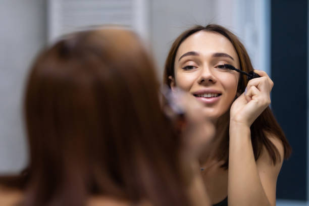 istock Beautiful young woman using mascara in bathroom 1304890632