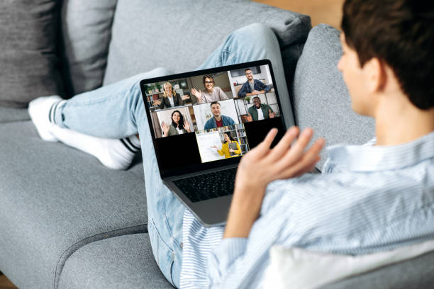 istock Distance learning. Caucasian guy, student, sitting on the couch at home, using a laptop, listening to an online lesson, different people and a teacher on the screen. Online education concept 1304899322