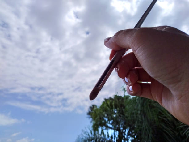 istock Hand holding a brush painting clouds in the sky 1304899529