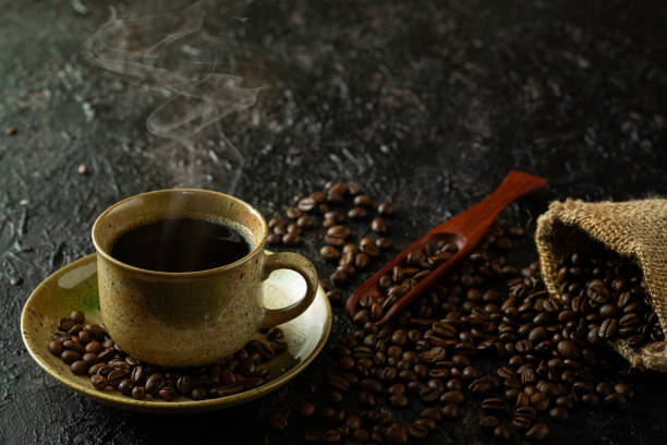 istock Hot black coffee with smoke for morning beverage menu in vintage brown ceramic cup with coffee beans roasted in burlap sack bag on dark grunge rustic table background. Flat lay with copy space. 1304900727