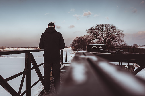 A man in warm, dark winter clothes, standing with his back on the bridge.