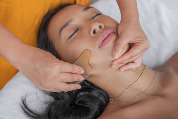donna indonesiana con gua sha facciale in una spa sanitaria - head massage massaging beauty treatment massage therapist foto e immagini stock