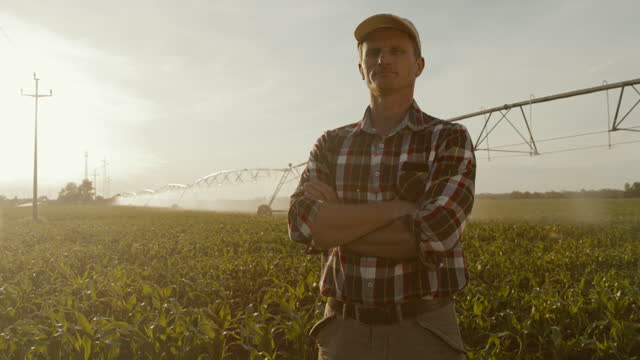 SLO MO Portrait of a farmer posing with arms crossed in the middle of irrigated field of corn