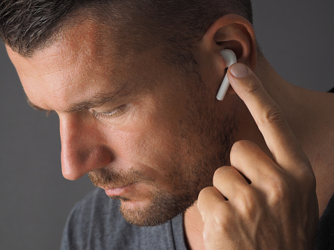 Man wearing wireless earphone and touching one earphone to control application. Close-up Headshot.