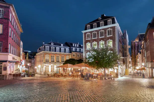 illuminated town square in the historic center of Aachen at blue hour with few people in street restaurant