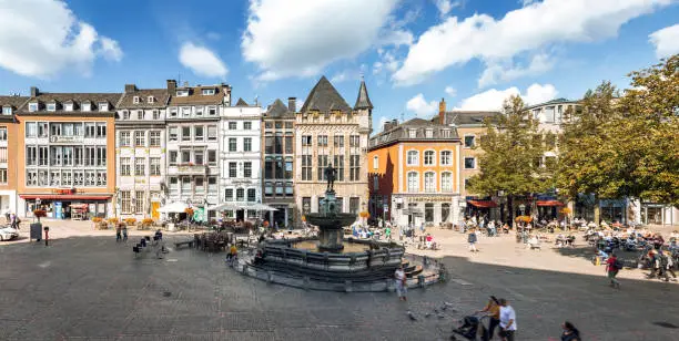 panoramic view on the facades of historic houses at Aachen market square with fountain at blue late summer day
