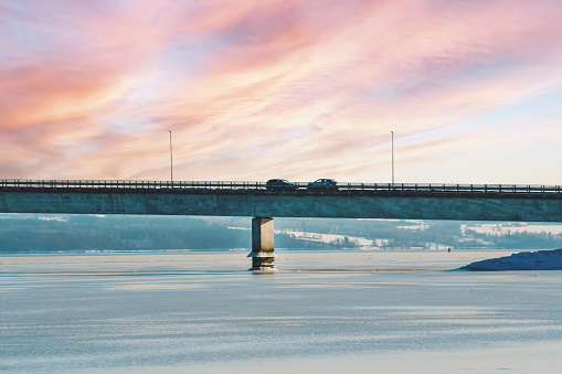 Highway bridge with traffic driving on it, spanning across a frozen bay on a winters evening.