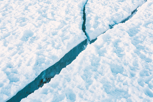 Large clean crack in sea ice with white snow on the top and clear blue ice beneath. Close up.