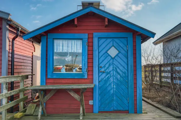 A typical Swedish summerhouse with a square window where part of the harbour is reflected into. The wooden facade and coarse table on the porch suggest a minimalism and a rustic, minimal lifestyle