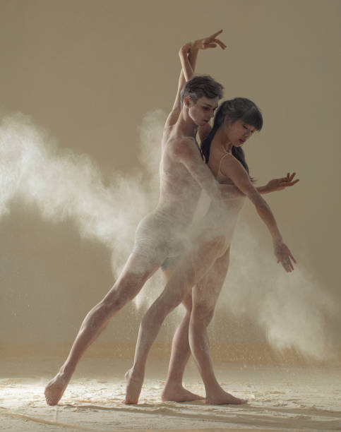 istock Two ballet dancers perform dance against background of white flour cloud in air. 1304929049