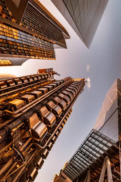 Highly detailed abstract wide angle view up towards the sky from a very low angle in the financial district of London City, UK and its ultra modern contemporary buildings with unique architecture on a bright sunny day. Shot on Canon EOS R full frame with 14mm wide prime lens for premium quality. Image is ideal for background with plenty of copy space for various concepts and ideas. Brown / golden toned in post production.