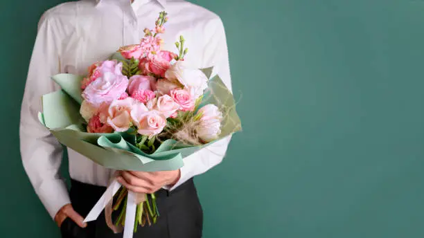 Man holding and giving a beautiful bouquet with flowers to woman on green background. Front view. Valentine's, women's, mother's day, love concept. Copy space. Place to the text.